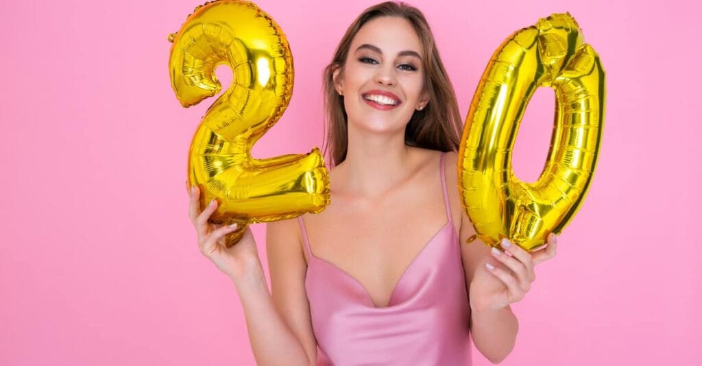 Young adult holding 20th birthday balloons