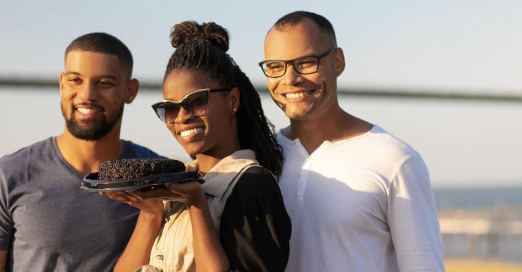 Smiling African American woman holding cake with 2 other men beside her